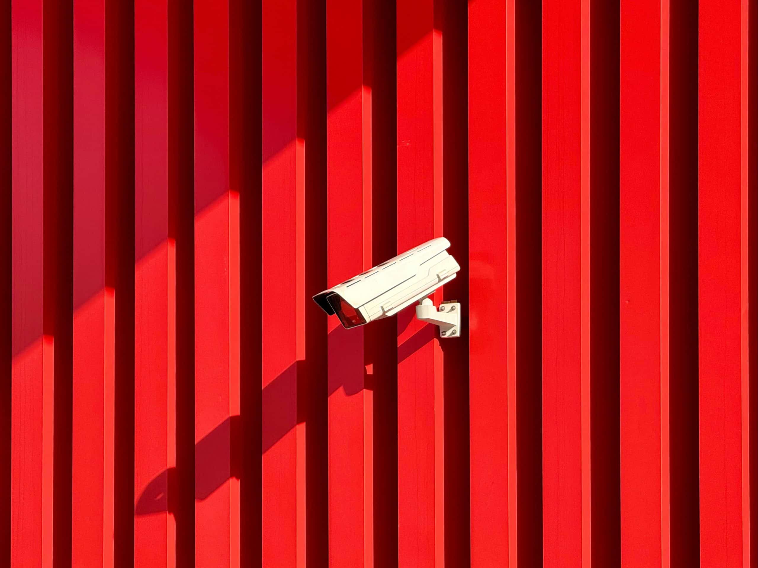 CCTV Camera on a red lined wall tracing people  - article explaining people tracing in the UK